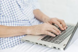 An elderly woman's hands typing on a laptop computer