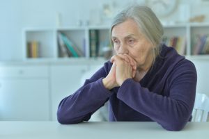 sad isolated senior sitting at a table in her home.