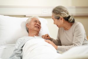 Senior asian woman visiting and talking to husband at bedside