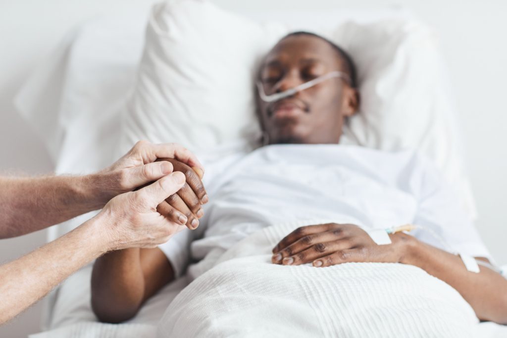 man lying in bed, family member holding their hand