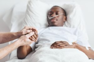 Close up of caring relative holding hand of African-American man lying in hospital bed