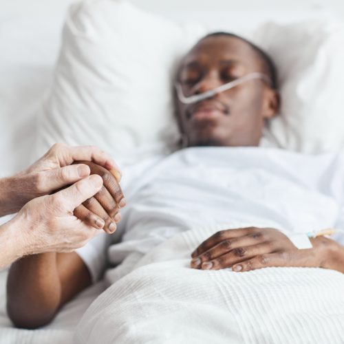 man lying in bed, family member holding their hand