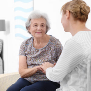 "senior woman sitting on sofa at home with caregiver"