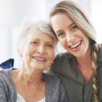 "portrait photo of senior woman and daughter smiling and sitting closely"