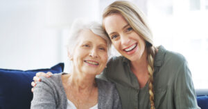 "senior woman and daughter smiling and sitting closely"