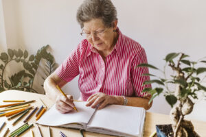 "senior woman drawing with coloured pencils in a colouring book on desk"
