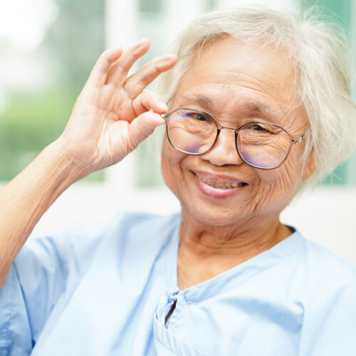 "Senior woman putting eyeglasses on her face close-up photo"