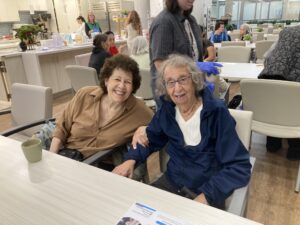 Two seniors sitting together at the Adult Day Program and smiling. 