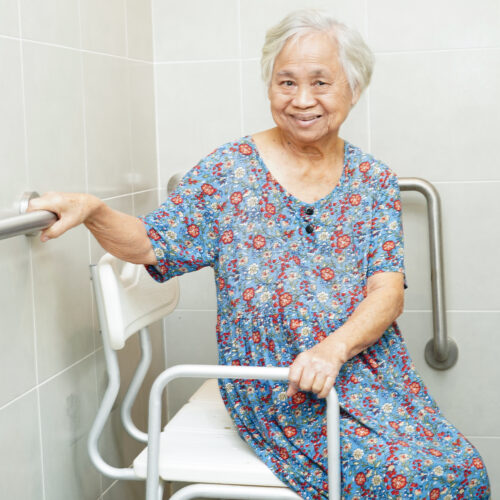 "senior woman sitting in bathroom, holding onto support rails"