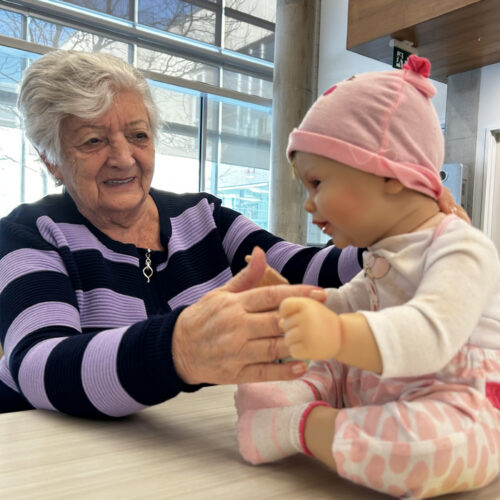 "Senior woman holds therapy doll on table"