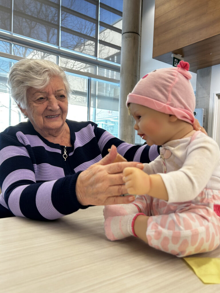 "Senior woman holds therapy doll on table"